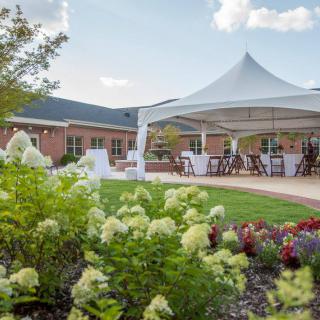 A beautifully set up outdoor event with a tent surrounded by lush gardens and blooming flowers.
