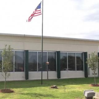 A building with a United States flag on a pole, surrounded by a lawn and trees.