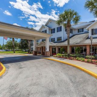 A building entrance with a covered driveway and landscaped surroundings on a sunny day.