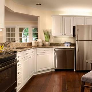 A modern kitchen featuring stainless steel appliances and white cabinetry with wood flooring.