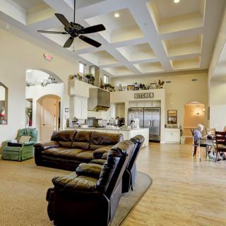 A spacious open-floor living room with a connected kitchen, featuring comfortable sofas, a ceiling fan, and high ceilings.