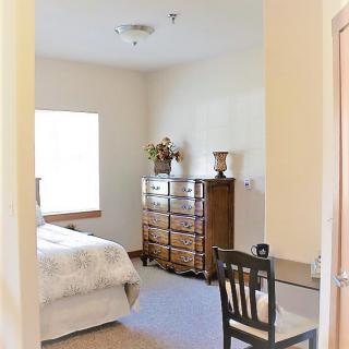 A cozy bedroom with a bed, dresser, and chair by the window.