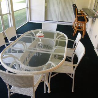 A cozy dining area with a glass table, surrounded by wicker chairs and adjacent to a counter with bar stools.