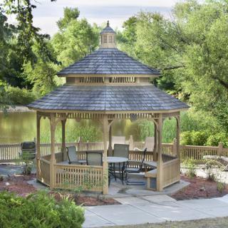 A wooden gazebo surrounded by trees near a peaceful lake.