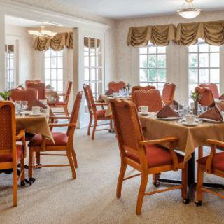 A well-lit dining room with arranged tables and chairs, featuring large windows and elegant decor.