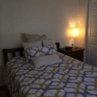 A cozy bedroom with a neatly arranged bed and a lit lamp on the nightstand.