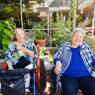 Two smiling elderly women enjoying a sunny day outside at a care facility.
