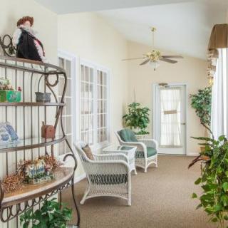 A cozy sunroom with rattan furniture, lush indoor plants, and a decorative shelf.