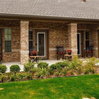 A brick house with a porch featuring columns and landscaping including plants and grass.