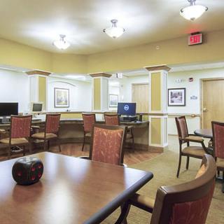 A spacious room with chairs, tables, and computers, featuring warm lighting.