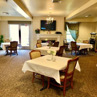 A cozy dining area with tables covered in white tablecloths, set around a fireplace and television.