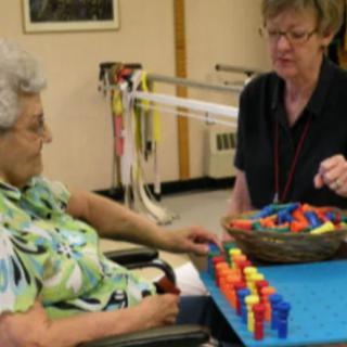 A caregiver assists a senior in a therapeutic activity session involving colorful pieces.