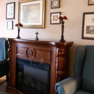 A cozy living room corner featuring a classic wooden fireplace mantle adorned with candlesticks, surrounded by framed pictures and comfortable armchairs.