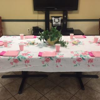 A beautifully arranged dining table ready for an event, featuring a floral tablecloth and pink accents.