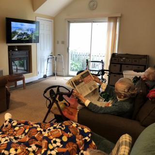 An elderly person reading a magazine in a cozy living room with a television on.