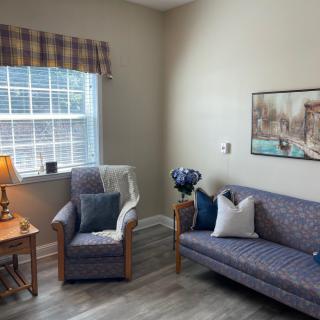 A cozy living room with a sofa, armchair, and artwork on the wall.