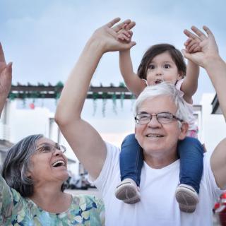 A joyful moment with grandparents giving a child a ride on shoulders outdoors.