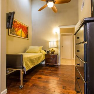 A cozy bedroom with a single bed, wooden floors, and warm lighting.