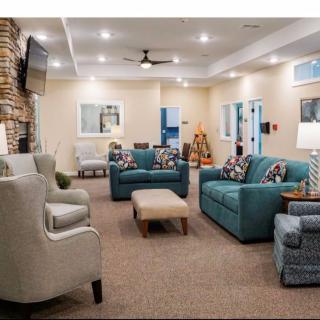 A modern living room featuring comfortable seating with blue and grey sofas, armchairs, and a TV mounted on the wall.