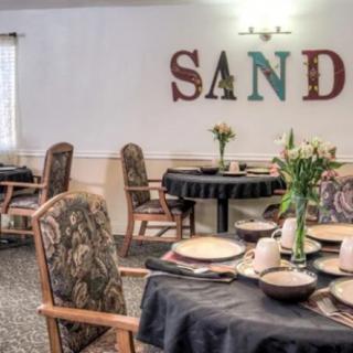 A cozy dining room setup with elegantly arranged tables and chairs, featuring floral centerpieces and decorative wall art.