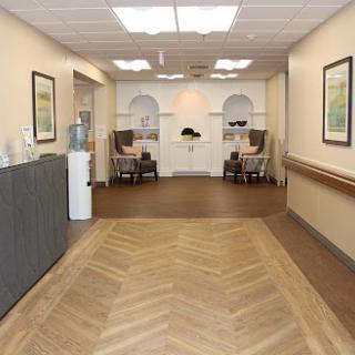 A well-lit hallway featuring wooden flooring and artwork on the walls, leading to a cozy seating area.