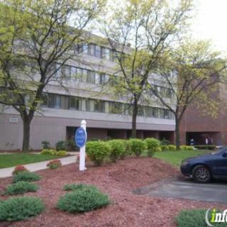 A four-story building surrounded by trees and landscaping with a car parked in front.