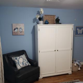 A cozy living room corner with a white wardrobe, black armchair, and decorative artwork on blue walls.