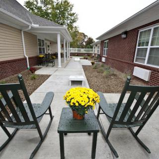 A peaceful patio area with two chairs, a small table, and a potted plant overlooking a walkway between buildings.