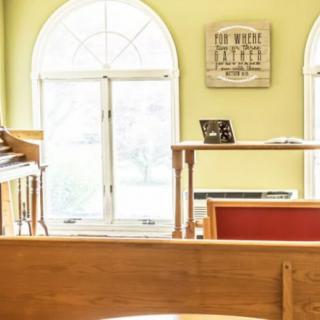 A peaceful church interior featuring wooden pews, an organ, and large arched windows.