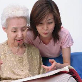 A young adult and an elderly person looking at a book together.