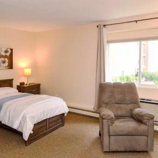 A cozy bedroom with a bed, recliner chair, and a window letting in natural light.