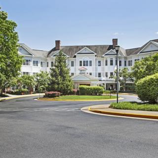 A residential-style building with a landscaped driveway and surrounding greenery.