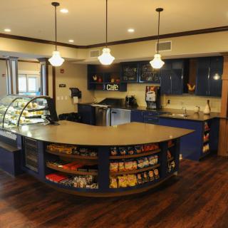 A modern cafe interior featuring a curved counter with a display case and snacks on wooden flooring.
