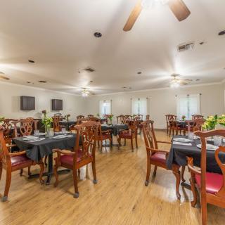 An elegant dining room with neatly arranged tables and chairs, featuring wooden floors and ceiling fans.