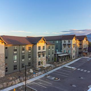 A modern hotel building with a parking lot, set against a mountainous landscape at sunset.