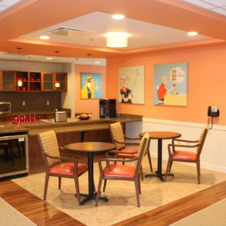 A cozy cafe interior with tables, chairs, and colorful artwork on orange walls.