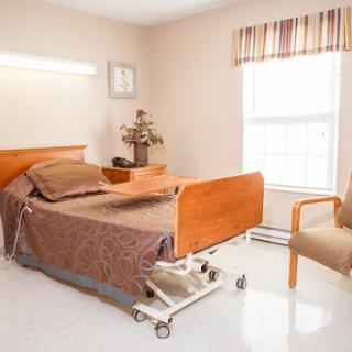 A well-lit hospital patient room featuring an adjustable bed, a chair, and natural light coming in through the window.