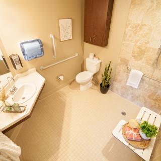 A modern bathroom featuring a sink, toilet, towel rack, and shower chair with beige walls and an indoor plant for decoration.