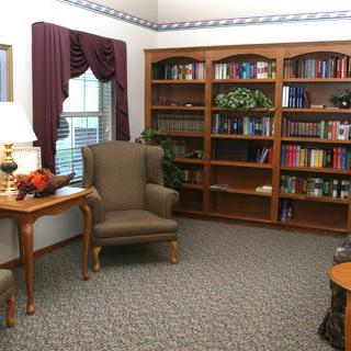 A cozy library corner with bookshelves, an armchair, and a small table by the window.