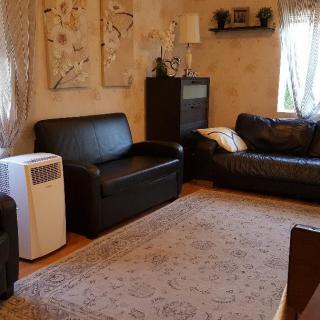 A cozy living room with dark leather sofas, a carpet, and an air conditioner.