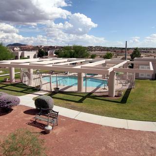 A scenic view of an outdoor swimming pool area with a pergola, surrounded by grass and under a partly cloudy sky.