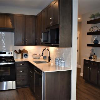 A modern kitchen with dark cabinetry, stainless steel appliances, and open shelving.