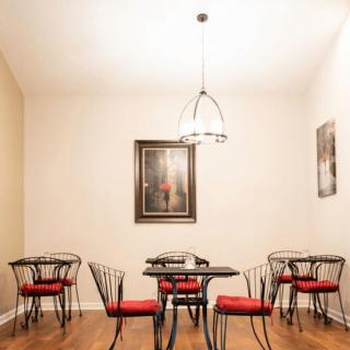 A cozy dining area with black metal tables and chairs featuring red cushions, adorned with artwork on the walls and a modern ceiling light.