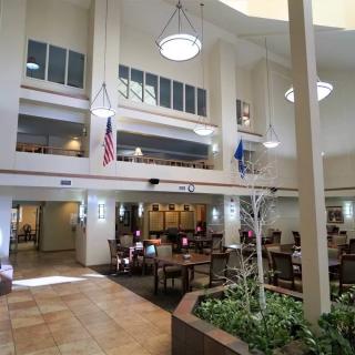 A spacious lobby with an atrium, featuring seating areas, flags, and indoor plants.