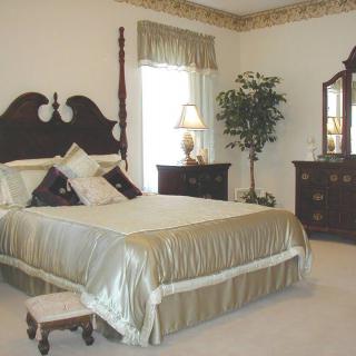 A traditional bedroom featuring a bed with a headboard, matching dresser and nightstand, a lamp, and decorative elements including a potted plant.