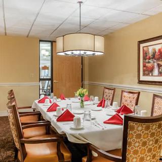A formal dining room with a neatly set table, featuring red napkins, elegant chairs, and a modern chandelier.
