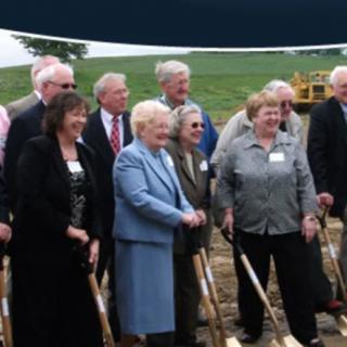 A group of people attending a groundbreaking ceremony, holding shovels outdoors.