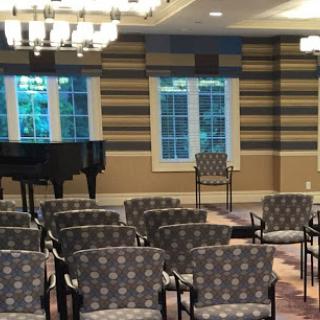 A spacious and inviting interior featuring upholstered chairs, a grand piano, and large windows allowing natural light.