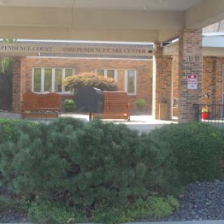 A view of a brick building with benches and greenery in the foreground.