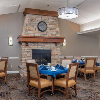 A cozy dining area featuring a stone fireplace and elegantly set tables with blue tablecloths.
